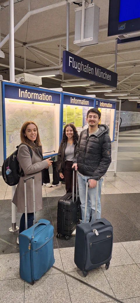 Three travellers posing with their luggage at Munich Airport.