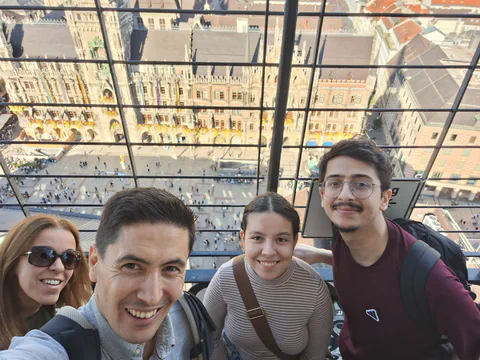 A group selfie beside windows overlooking Munich's rooftops.